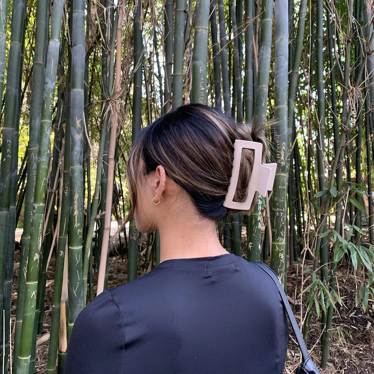 woman with coloured hair wearing a large claw clip in a cream vanilla colour against a bamboo background
